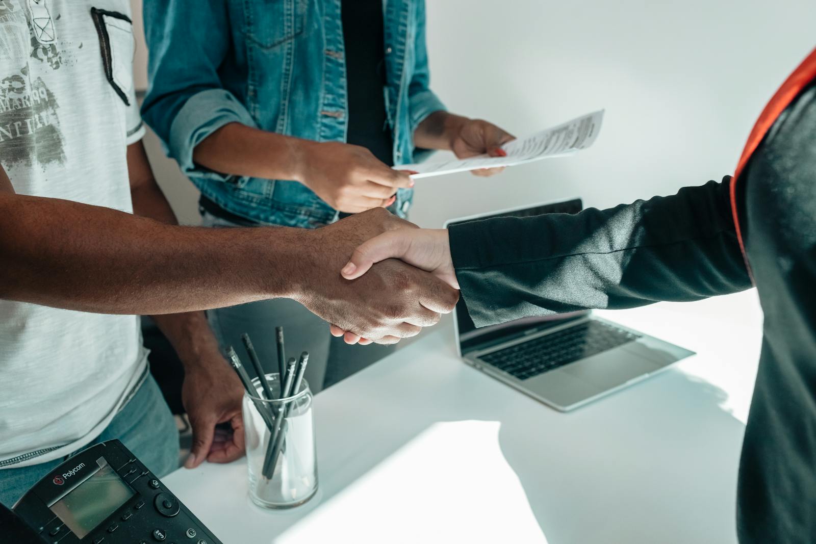 Two business professionals engaging in a handshake agreement in a modern office environment with documents present.